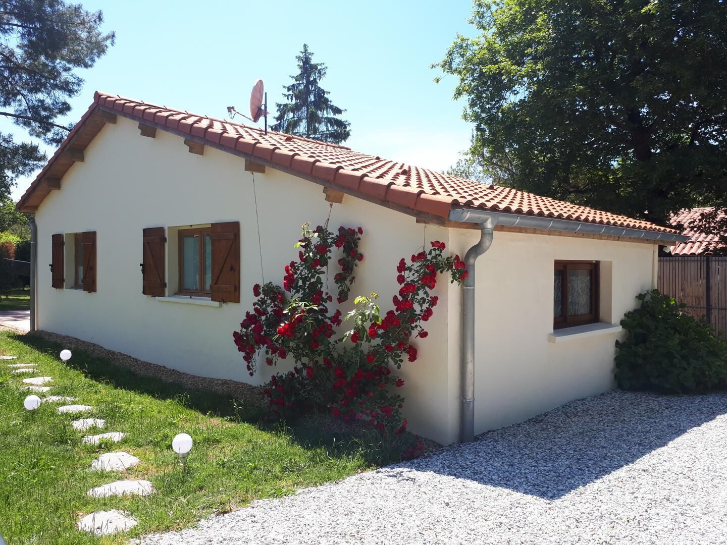 A single-story house with a tiled roof, a satellite dish, and a garden with red flowers.