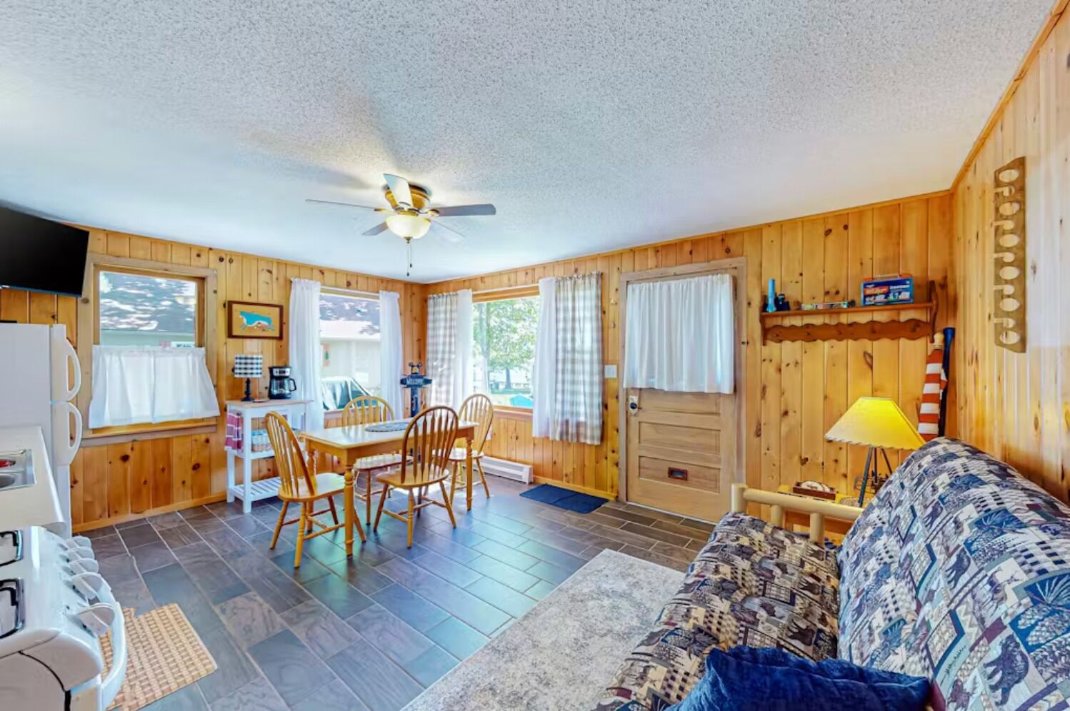 A cozy cabin interior with a dining area, a sofa, and a ceiling fan.