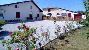 A two-story house with a gravel driveway and a garden with pink flowers.