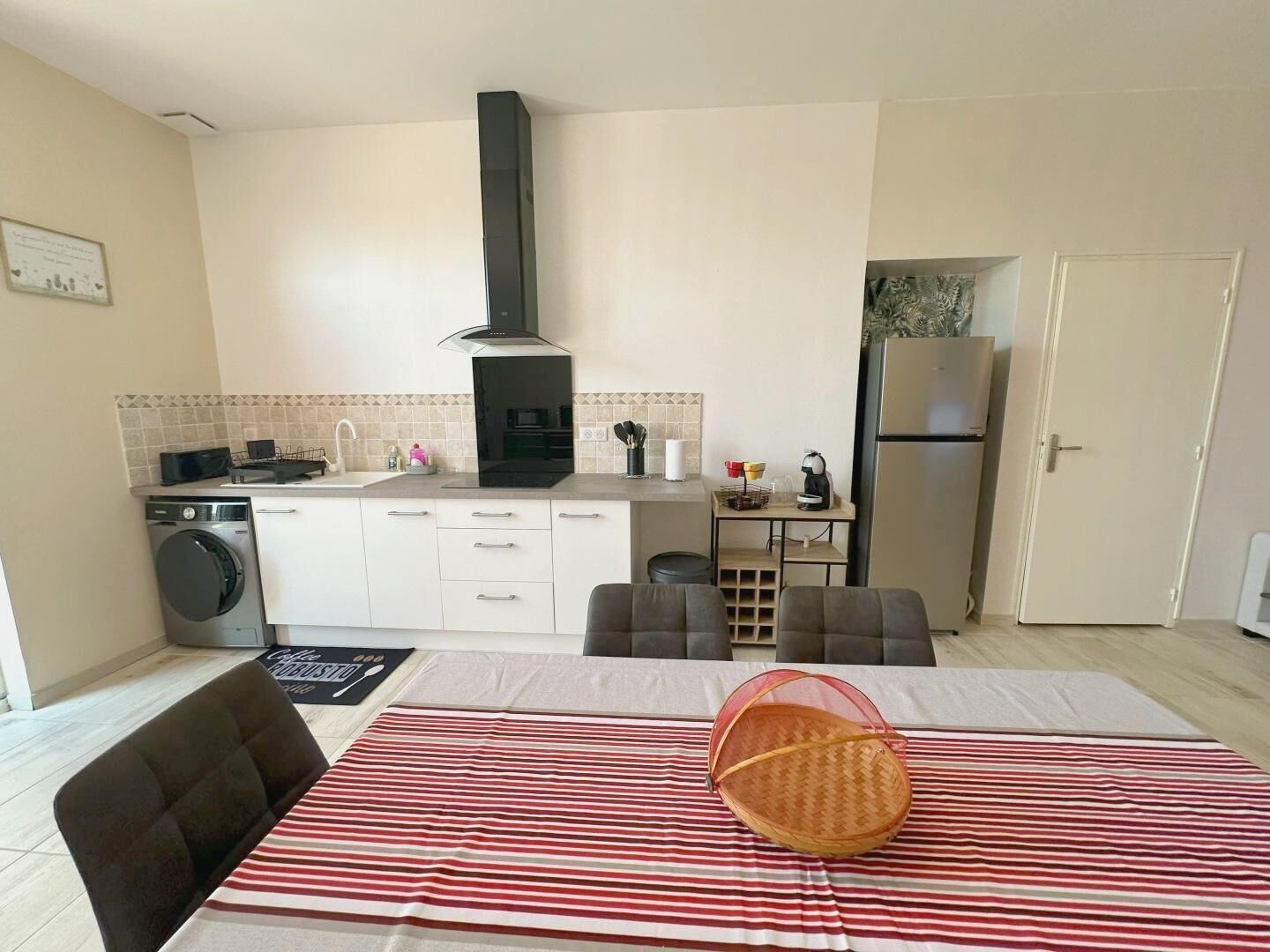A compact kitchen with a washing machine, a stove, and a refrigerator. There is a dining area with a table and chairs.