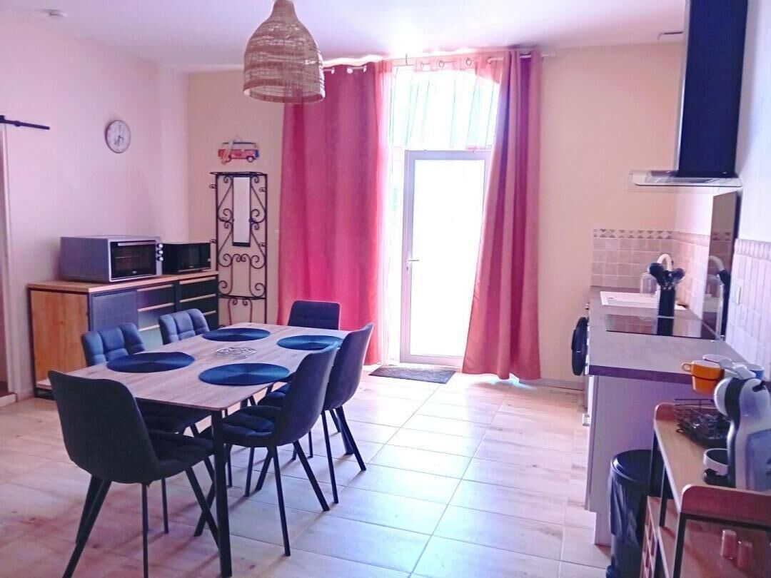 Una cucina funzionale con microonde, tostapane e lavello. Un tavolo da pranzo con sedie è posizionato vicino a una finestra con tende rosa.
