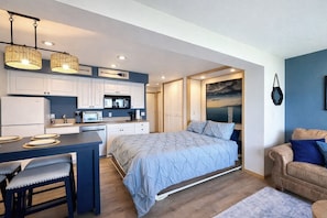 A compact bedroom with a bed, a small kitchenette, and a seating area with a couch.