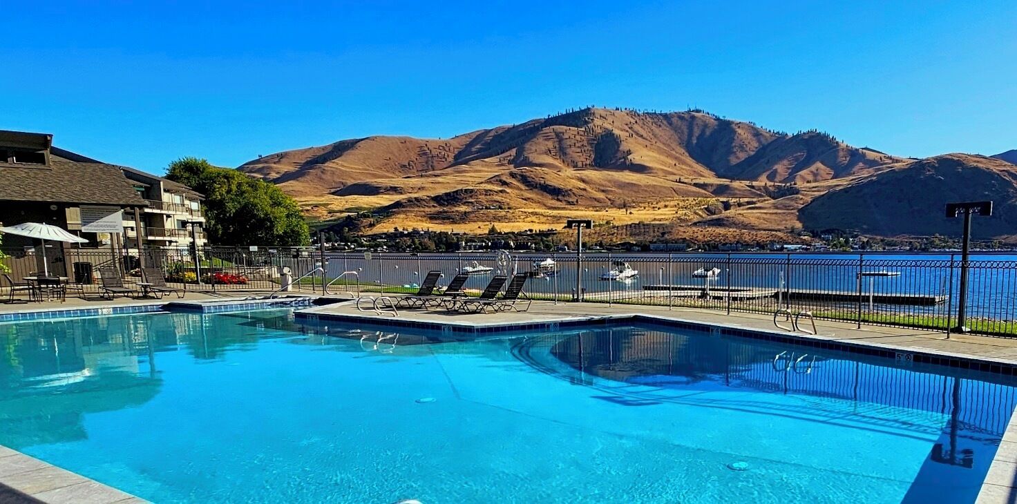 A swimming pool with lounge chairs, a fenced deck, and a view of mountains.