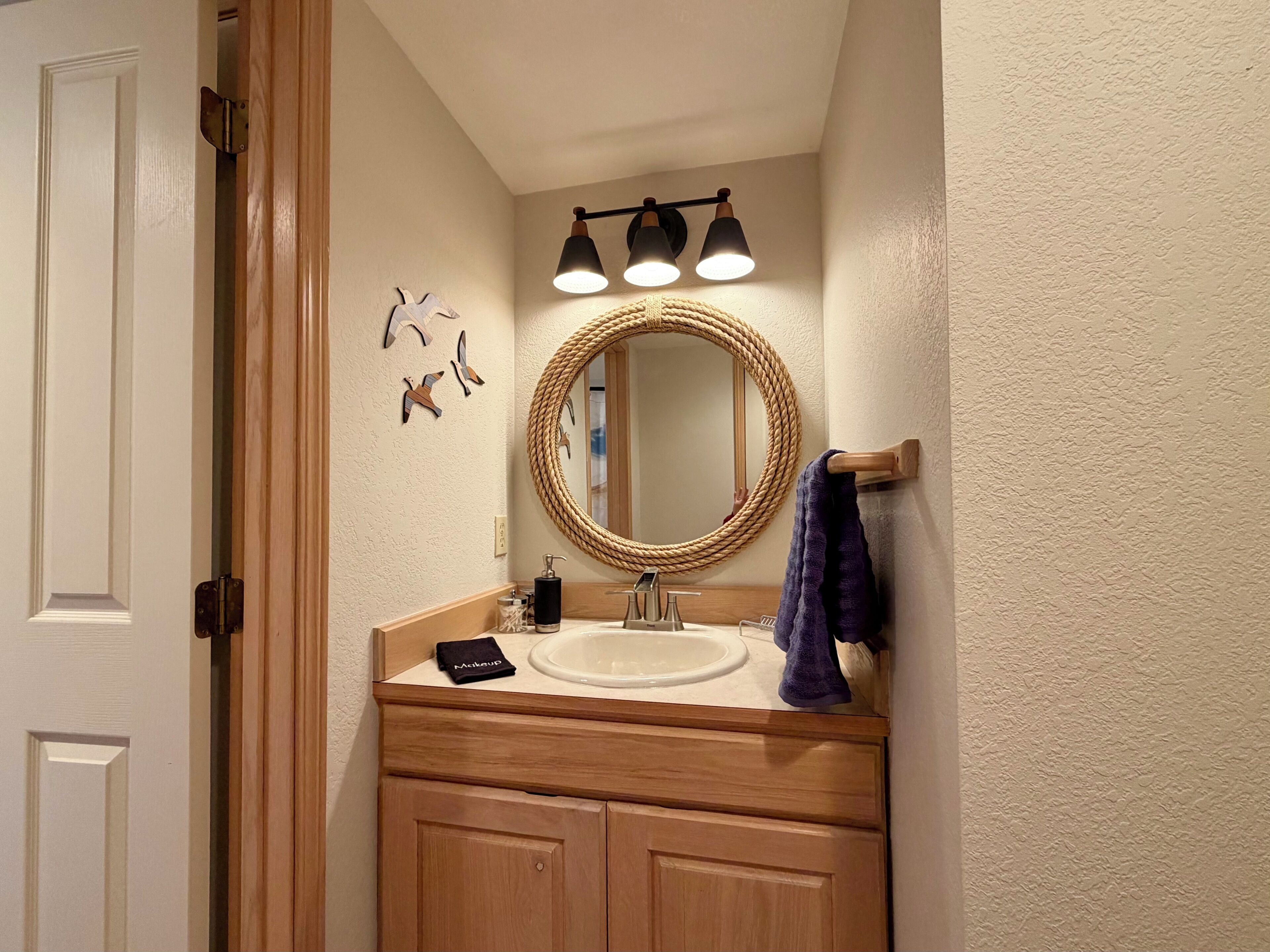 A bathroom with a wooden vanity, a round mirror, a sink, and a towel rack.