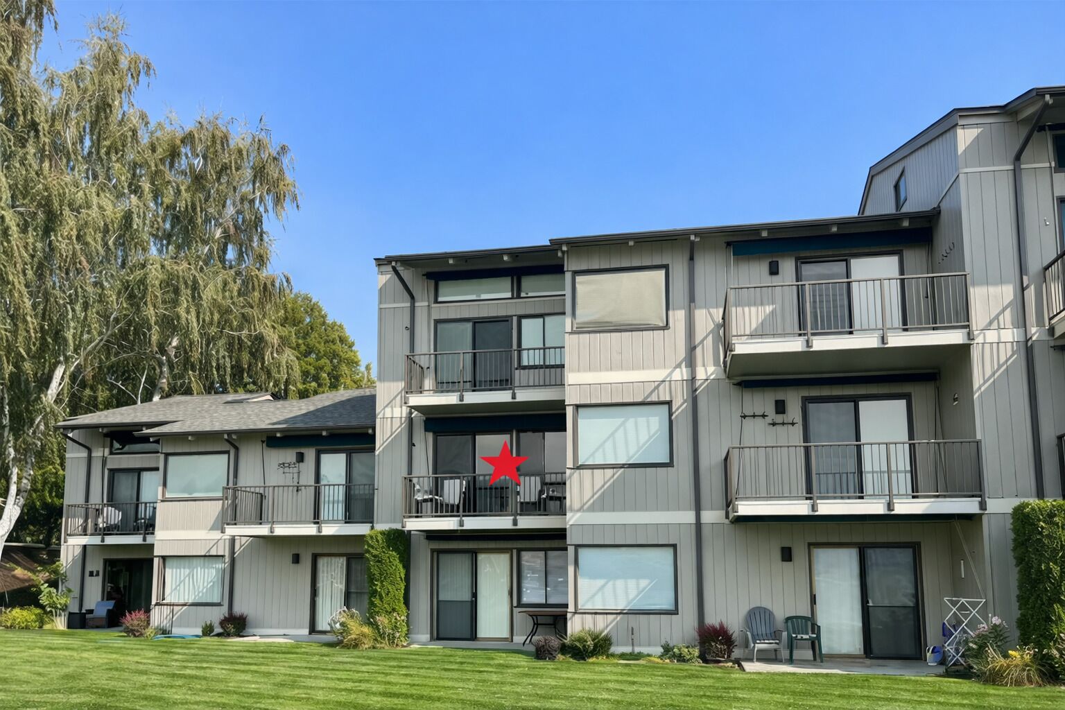 En flervåningsbostadsbyggnad med balkonger, stora fönster och en välskött gräsmatta.