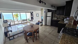 Een moderne keuken met een ruim kookeiland, een eethoek met uitzicht op de oceaan, en een woonkamer met een bank en salontafel.