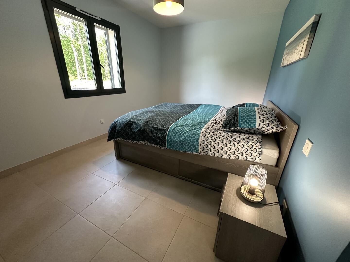 A bedroom with a bed, a bedside table, and a window.