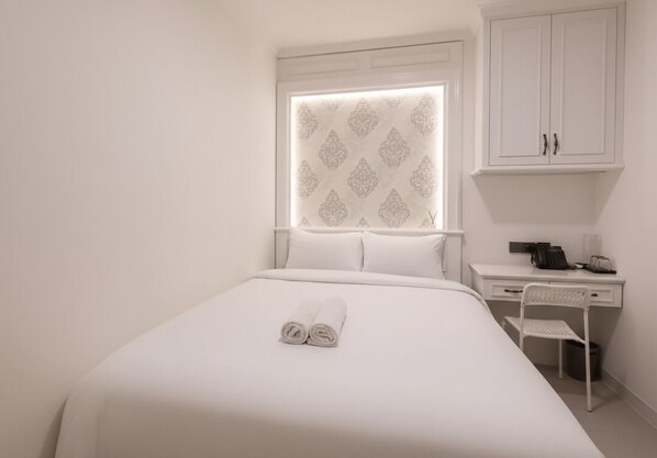 A neatly made bed with rolled towels, a desk with a chair, and a cabinet. - Wyneth Hotel Airport (Tangerang)