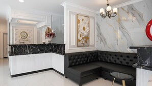 A modern living room with a black sectional sofa, a marble accent wall, and a black and white marble coffee table. - Wyneth Hotel Airport (Tangerang)