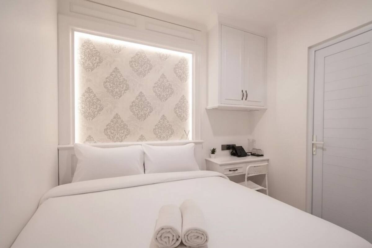 A hotel room with a neatly made bed, a desk with a phone, and a wardrobe.