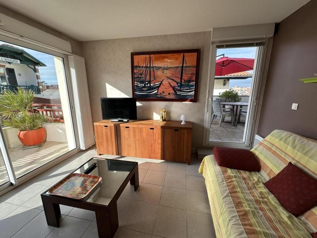 A living room with a sofa, a coffee table, a TV, and a wooden cabinet. There is a painting on the wall and a view of the outside through a glass door.