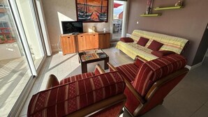 Una sala de estar con sofá, sillón, televisor, aparador de madera y obra de arte en la pared.