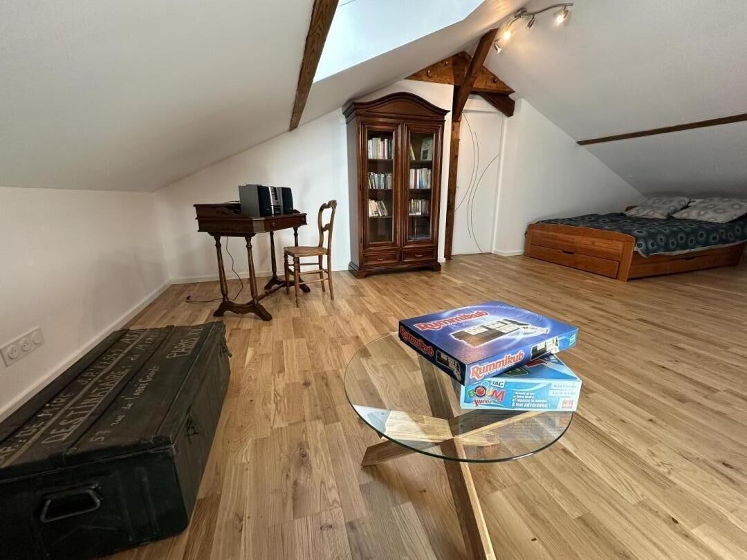 Une petite pièce mansardée avec un plancher en bois, une table en verre, une armoire en bois, un lit et un bureau avec une chaise.