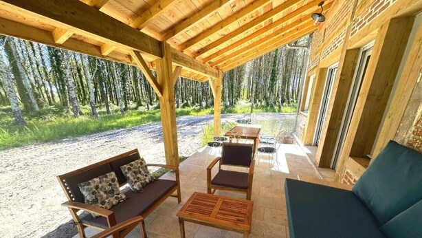 A covered outdoor seating area with wooden furniture and a view of a forest. - La résinière - MAGESCQ - Gîte (MAGESCQ)