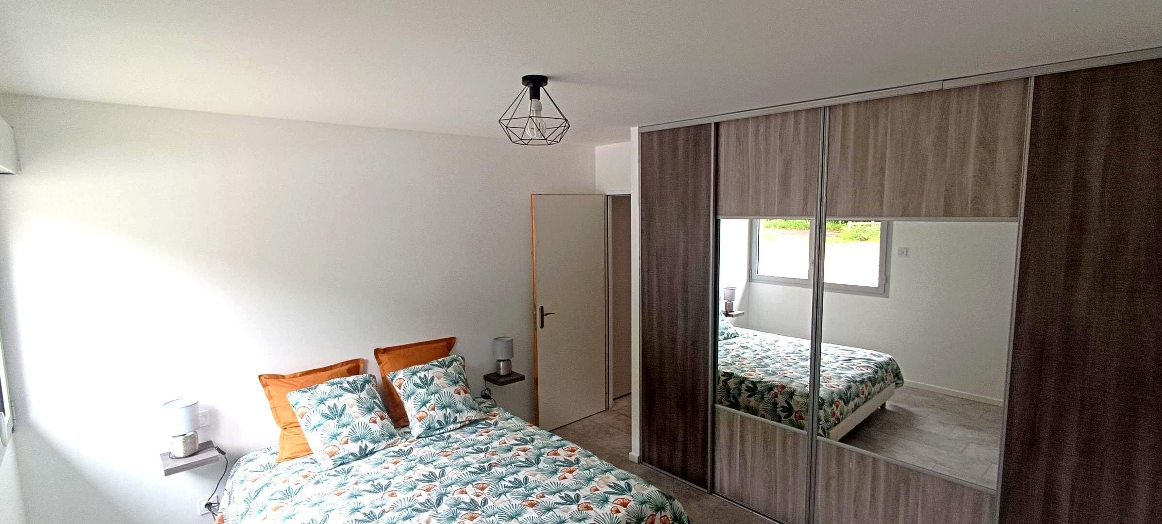 A bedroom with a bed, a bedside table, a lamp, a wardrobe, and a window.