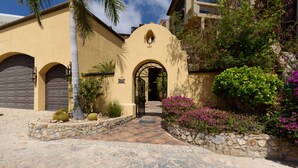 A Mediterranean-style building with a stone-paved entrance, arched garage doors, and a decorative archway. - Spacious 3 Bedrooms with Private Pool in Cabo’s Pedregal (Cabo San Lucas)
