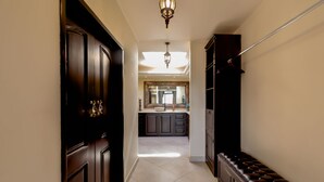 A hallway with a dark wooden door, a bench, and a kitchen area in the background. - Spacious 3 Bedrooms with Private Pool in Cabo’s Pedregal (Cabo San Lucas)