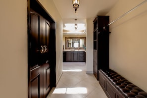 A hallway with a dark wooden door, a bench, and a kitchen area in the background. - Spacious 3 Bedrooms with Private Pool in Cabo’s Pedregal (Cabo San Lucas)