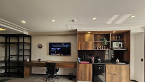 A modern office space with a wooden desk, a computer monitor, a black office chair, a built-in kitchen area with a microwave, and a small refrigerator. - Epic Suite 209 Deluxe Aeropuerto (Pereira)