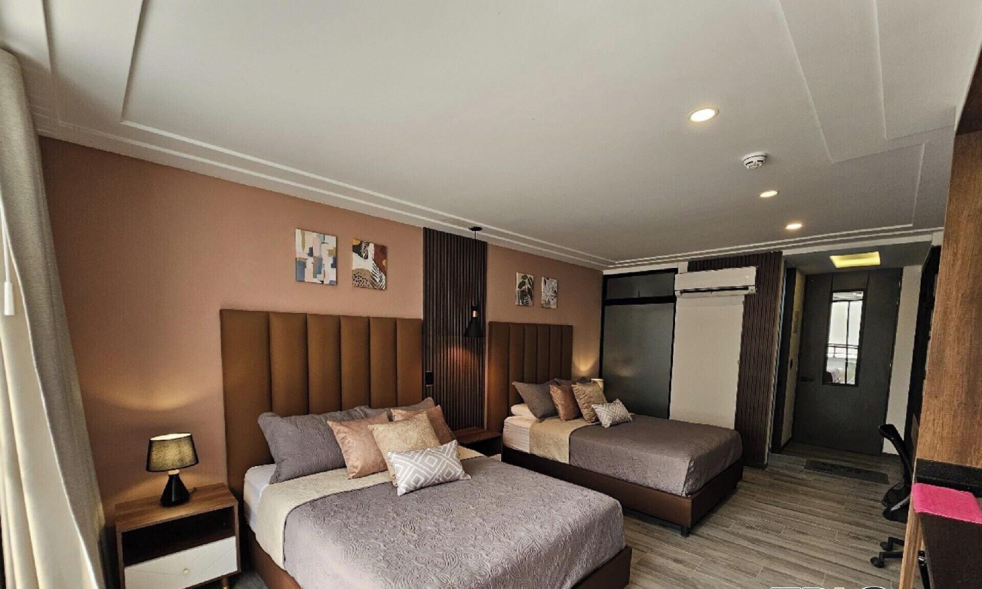 A hotel room with two beds, a nightstand, a lamp, and artwork on the walls.