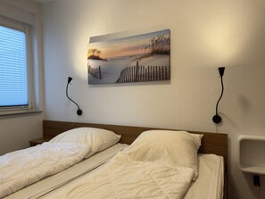 Un dormitorio con dos camas, un cuadro de una playa y una lámpara fijada a la pared.