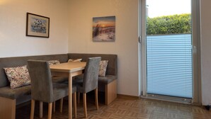 A dining area with a table, chairs, and a bench. There are two framed pictures on the wall. - Bungalow mit Garten in Dornumersiel (Dornum)