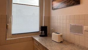 A kitchen with a window, a toaster, a coffee maker, and a painting on the wall. - Bungalow mit Garten in Dornumersiel (Dornum)