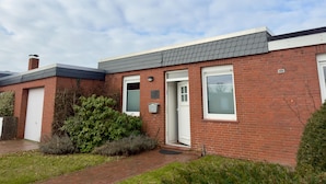 A two-story brick house with a white door, a small window, and a chimney. - Bungalow mit Garten in Dornumersiel (Dornum)