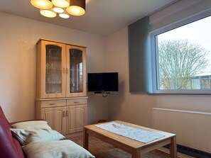 Una habitación con un armario de madera, un televisor, una mesa con camino de mesa, una ventana con persianas y un radiador.