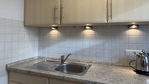 A kitchen with a stainless steel sink, granite countertop, and wooden cabinets. - Bungalow mit Garten in Dornumersiel (Dornum)