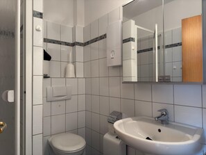 Un baño con inodoro, lavamanos, espejo y toallero.