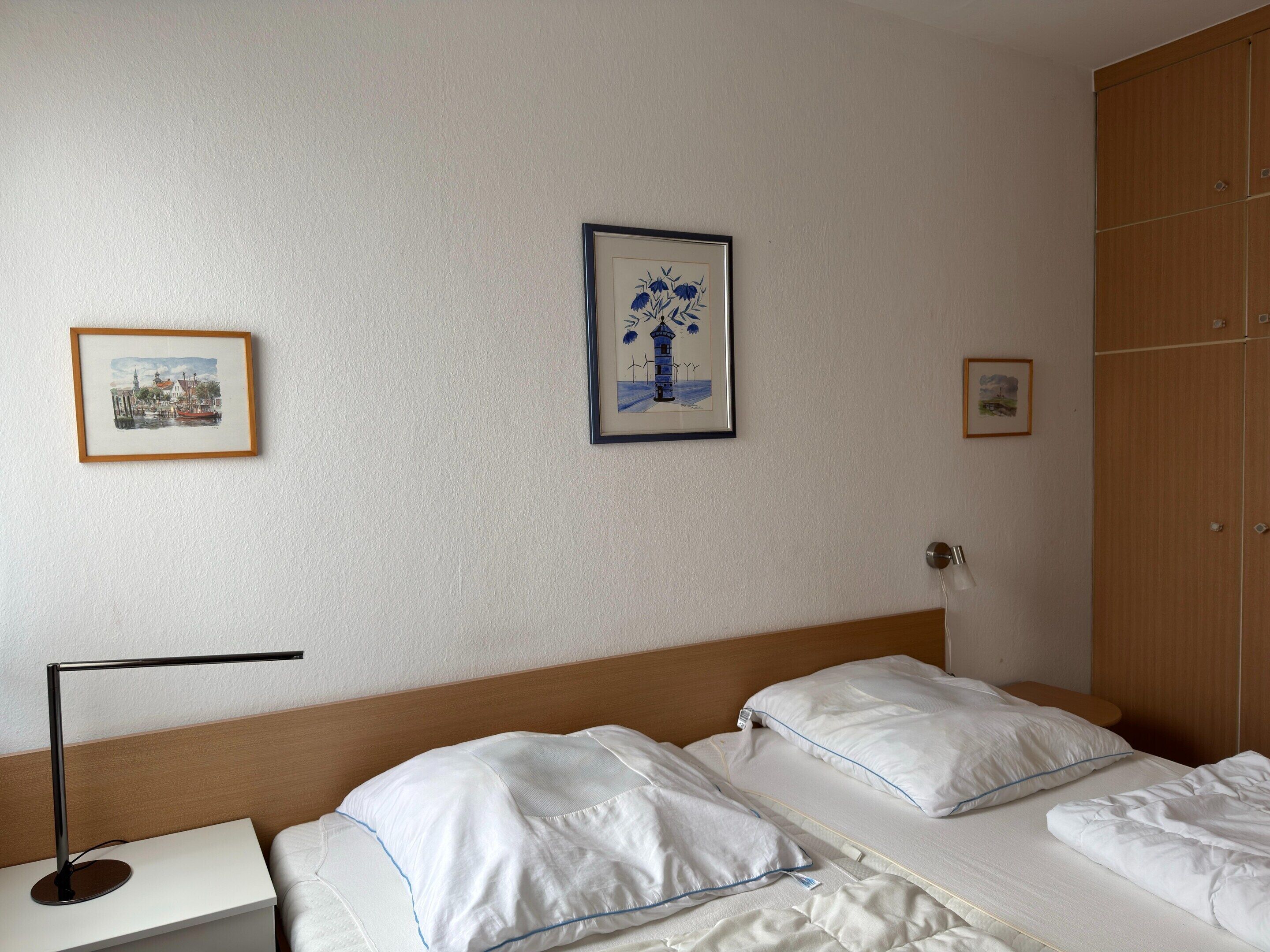 Una habitación de hotel con dos camas, una mesita de noche, una lámpara de escritorio y cuadros en la pared.