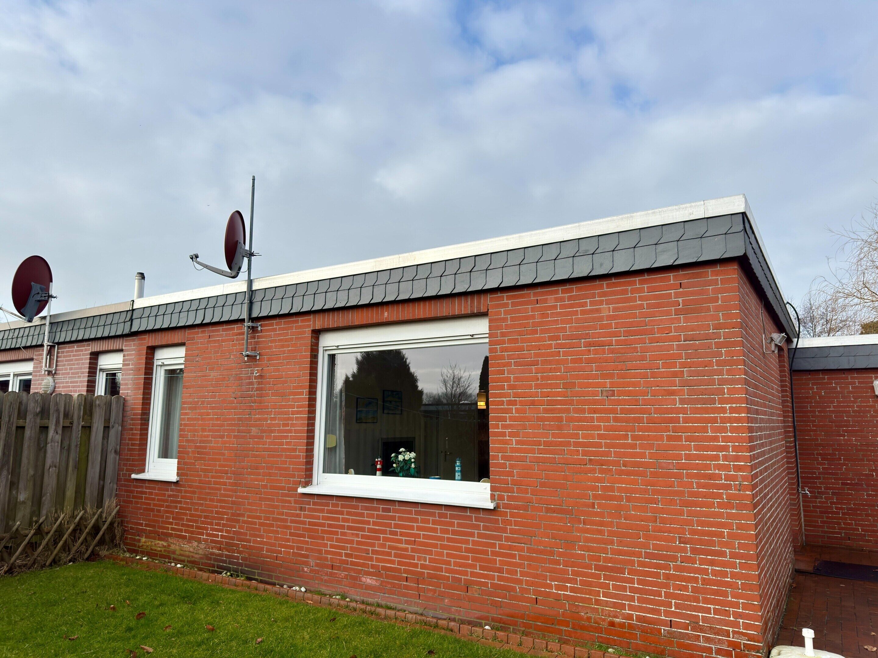 A red brick building with a white window, a satellite dish, and a wooden fence.