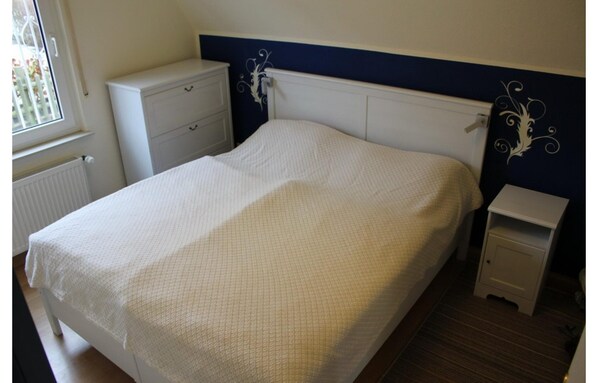 A single bed with a white bedspread, a white bedside table, and a white nightstand. - Ferienhaus in Dornumersiel (Dornum)