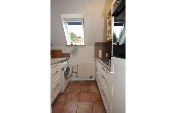 A compact kitchen with a built-in washer, a window with a view, and a radiator. - Ferienhaus in Dornumersiel (Dornum)