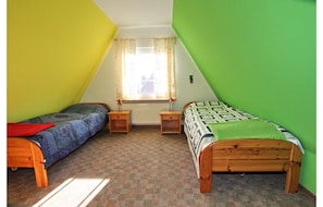 A room with two single beds, a window with curtains, a radiator, and a wooden floor. - Ferienhaus in Dornumersiel (Dornum)