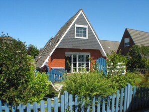 A house with a gabled roof, a front door, and a blue picket fence. - Ferienhaus in Dornumersiel (Dornum)
