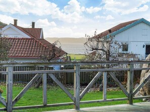 A wooden deck with a view of a lake, a white building with a red roof, and a blue building with a white roof. - 3 Person Holiday Home in Hunnebostrand (Hunnebostrand)