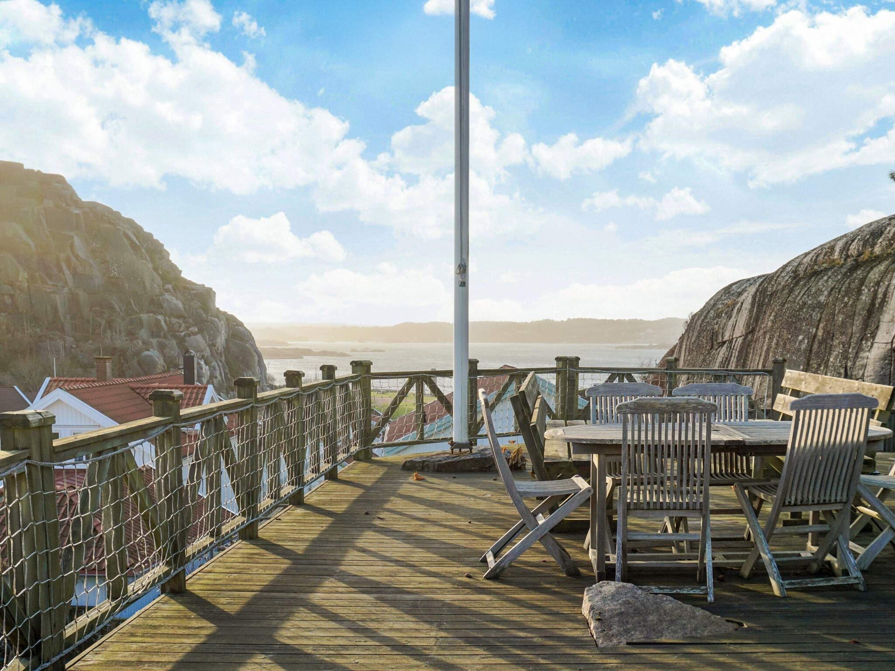A wooden deck with a table and chairs, overlooking a body of water and rocky cliffs.