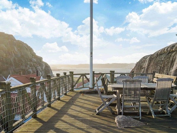 A wooden deck with a table and chairs, overlooking a body of water and rocky cliffs. - 3 Person Holiday Home in Hunnebostrand (Hunnebostrand)