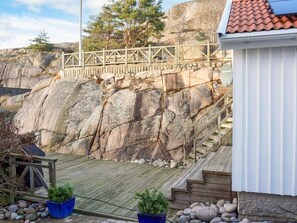 A wooden staircase leading up to a rocky cliff, a wooden deck, and a white building with a red roof. - 3 Person Holiday Home in Hunnebostrand (Hunnebostrand)