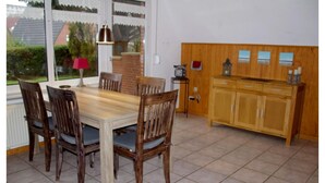 Ein Essbereich mit einem Holztisch und Stühlen, einer Kommode mit Schubladen, einer Lampe und Blick ins Freie.