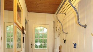 Ein Korridor mit Holzboden, einer weißen Tür mit Glasfeldern, einem Metallregal mit Regenschirmen und einem Spiegel an der linken Wand.