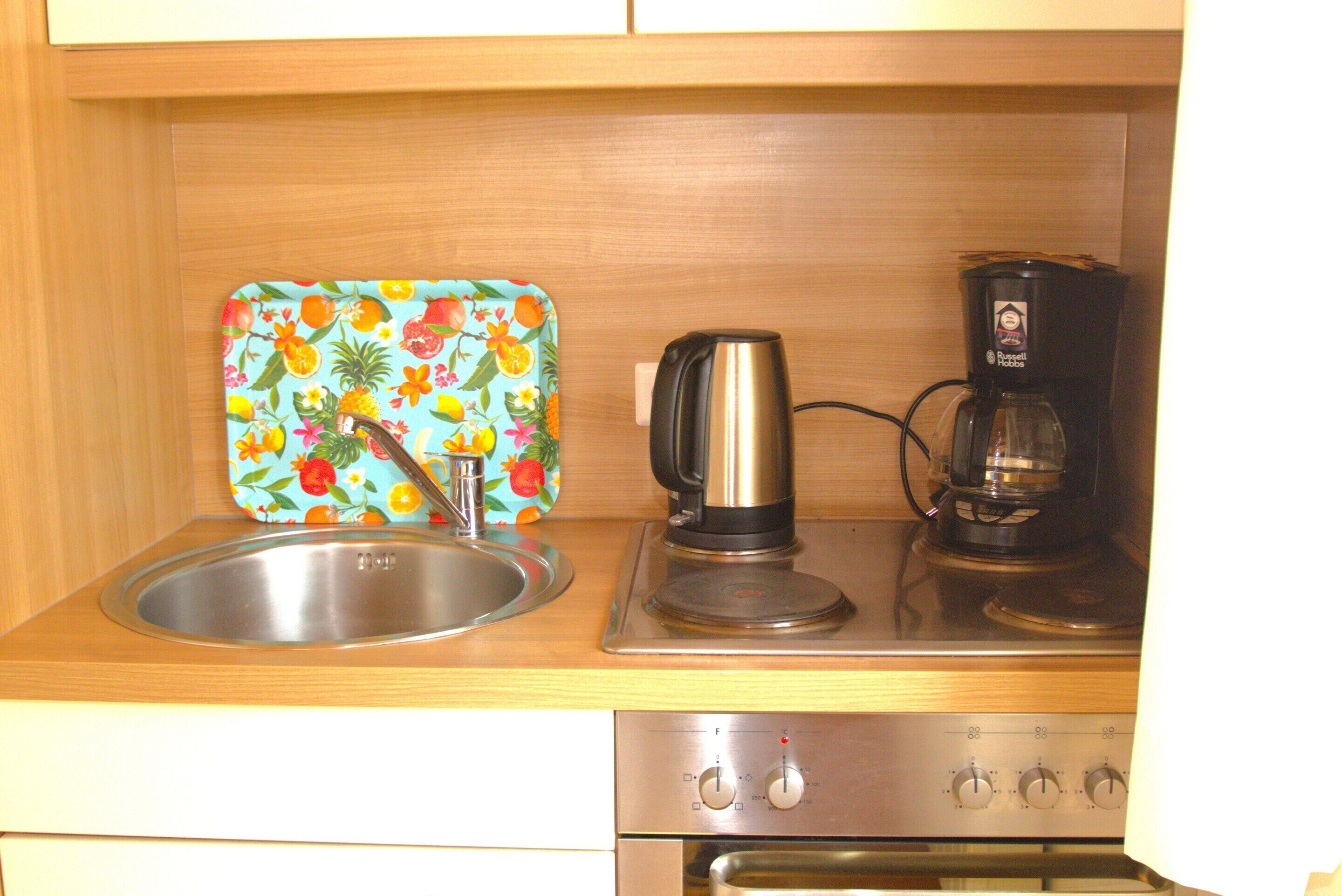 A kitchen with a stainless steel sink, a kettle, and a coffee maker on the countertop.