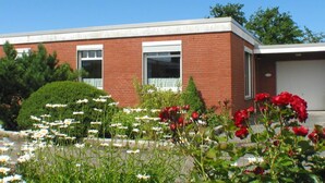 Un edificio in mattoni di due piani con un garage, immerso in giardini curati e ricchi di fiori e siepi.