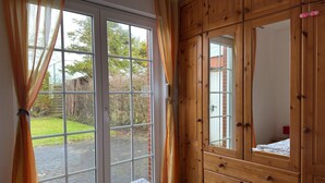 A bedroom with a large window, wooden wardrobe, and a bed. - Bungalow in Strandnaehe, Dornumersiel (Dornum)