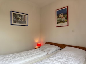 A bedroom with two beds, a nightstand with a red lamp, and two framed pictures on the walls. - Bungalow in Strandnaehe, Dornumersiel (Dornum)
