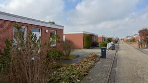 A residential street with brick houses, a paved sidewalk, and a row of trash bins. - Bungalow in Strandnaehe, Dornumersiel (Dornum)