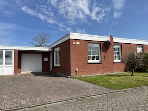 A two-story brick building with a garage, a satellite dish, and a small lawn. - Bungalow in Strandnaehe, Dornumersiel (Dornum)