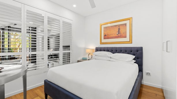 A bedroom with a bed, a nightstand, a ceiling fan, a window with blinds, and a framed picture on the wall. - 1-bed Unit With Alfresco Dining and BBQ (Sydney)